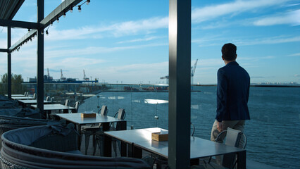 Successful businessman walking terrace in sea view cafe. Calm morning breakfast