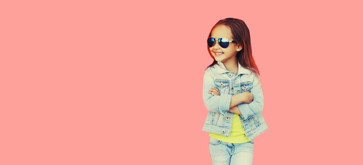 Portrait of stylish little girl child wearing sunglasses, jeans jacket on pink background