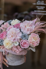 Beautiful spring flowers in box on woman hands. Preserved arrangement in grey round box. Women's day.