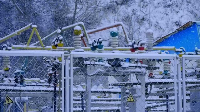 Transformer substation with wires, insulators, electric busbars, power transformer, switchgears, switching equipment in winter during snowfall. Snowflakes slowly and beautifully fly way down. Slow mo