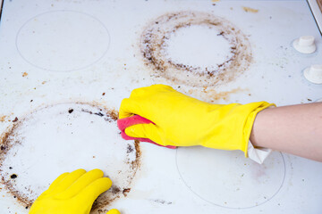 Man cleaning ceramic modern stove or hob with detergent agent. Hand in yellow gloves clean stove...