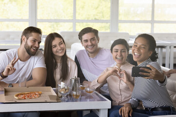 Happy multiethnic friends taking selfie on smartphone in cafe, shooting self video, holding mobile phone, smiling, laughing, posing at table with pizza, hot drink, having fun