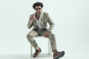 curly hair guy with sunglasses adjusting shirt collar and sitting
