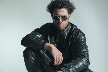 Obraz premium confident man with sunglasses wearing leather outfit and posing with elbow on knee