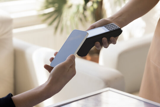 Hand of waitress holding contactless payment terminal, connecting gadget with cellphone of customer in cafe. Buyer using mobile bank service, paying bill in restaurant.
