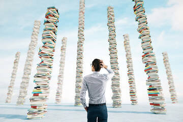 Knowledge and education concept with man back view looking on high stacks of books on abstract concrete surface and blue sky background - Powered by Adobe