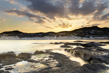 Sunrise behind the mountain in a fishing village. There are clouds in the sky. The sea has silk effect by low exposure and enters between the rocks. White village. Fog effect. Blurred areas
