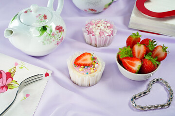 Round cheesecake with strawberry slice, tea party with desserts, space for text. Cheesecakes with colored sprinkle balls, pink frosting, bowl of fresh strawberries, tea utensils, set table, copy space