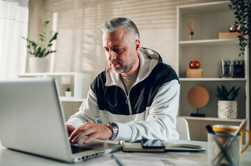 Fototapeta premium Middle aged man a laptop while working in a home office