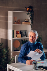 Gray haired middle aged man working in a home office with paper documents