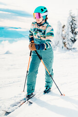 Woman in skiing clothes with helmet and ski googles on her head with ski sticks. Winter weather on...