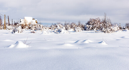 Field covered with deep snow at the edge of the village