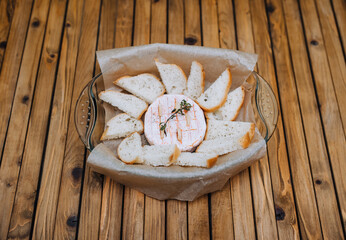 Round camembert cheese with thyme and fresh bread croutons lie in a glass plate, shape on a wooden background, table. Photo close-up of food.