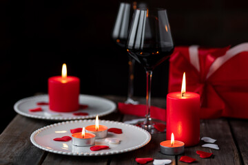 Saint Valentine's Day celebration. Red burning candles, hearts, gift box, postcard on dark wooden background. Happy holiday . Table decor for festive dinner, romantic atmosphere