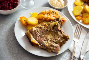 Hearty homemade lunch of slices of roast pork served with baked potatoes and cabbage stewed with vegetables..