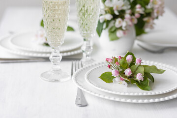 Beautiful table decor for a wedding dinner with a spring blooming apple tree flowers. Celebration of a special event. Fancy white plates, wineglasses