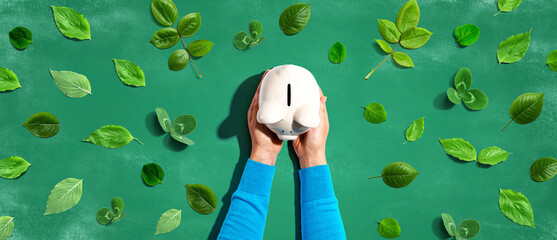 Person holding a piggy bank with green leaves - flat lay