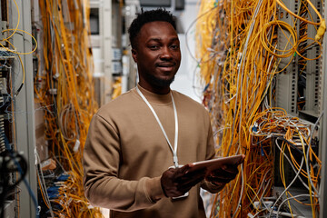 Waist up portrait of black man as system administrator standing in server room and smiling at camera