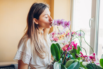 Happy woman kissing blooming purple Andorra orchid holding pot. Girl gardener taking care of home...