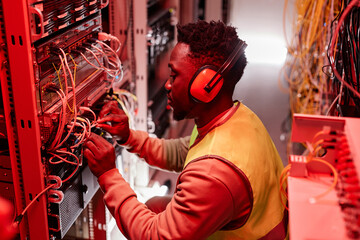Side view portrait of technician setting up network in server room and wearing ear protection lit...