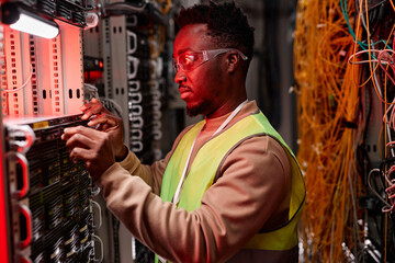 Side view portrait of network technician inspecting servers in data center lit by red neon light