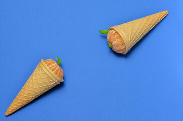 two waffle cones with tangerine on a blue background, flat lay