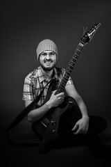 Fototapeta premium happy musician, bearded guy in checkered shirt sitting on ground with guitar, black and white photo