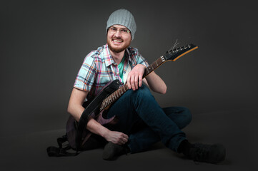 happy musician, bearded guy in checkered shirt sitting on ground with electric guitar. Guitarist, artist, composer, rocker, star.