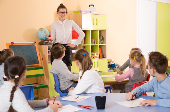 Elementary age group of pupil listening smiling teacher at whiteboard at class