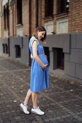 Fototapeta premium Happy pregnant woman chilling and having fun while walking in the city in a midi blue vintage dress. Happiness all around