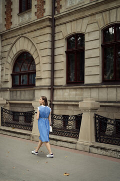 Beautiful young pregnant woman in a blue dress walking through the city streets using a smartphone.
