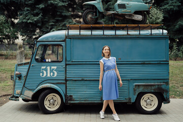 Charming pregnant womanin in a blue retro dress posing near a vintage bus with copy space.