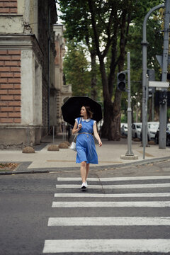 Pretty woman, in a blue dress, with a white purse and an umbrella passing the crosswalk