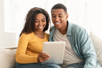 Fototapeta premium Cheerful young african american family look at tablet, make video call, surfing in internet, chatting online