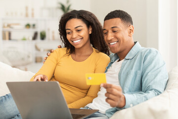 Cheerful young african american guy and woman use credit card and laptop, check bank financial account