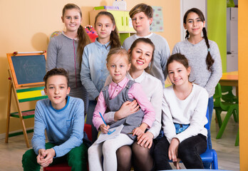Portrait of friendly positive group of pupils with female teacher sitting in schoolroom