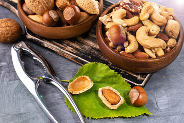 Fototapeta premium Top view of various nuts in wooden bowls and nutcracker on gray surface