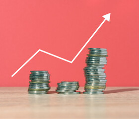 A stack of metallic coins and a graph on a red background. Income growth in business, high profitability