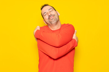 Bearded hispanic man completely excited and self-absorbed hugging himself showing he loves himself very much isolated over yellow background.