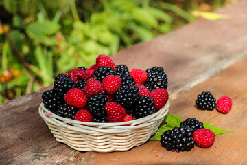 Organic raspberries and blackberries in a basket on a wooden background in summer garden