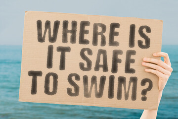 The question " Where is it safe to swim? " is on a banner in men's hands with blurred background. Inflatable. Young. Buoy. Nature. Summer. Travel. Kid. Protection. Baby. Little. Childhood