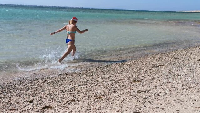 a girl in a New Year's hat runs through the water on the Red Sea.
