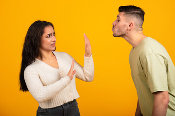 Millennial arab guy kissing woman, lady doing stop sign with hands, isolated on orange background