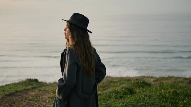 Stylish girl looking sunset standing on green hill near ocean. Model posing