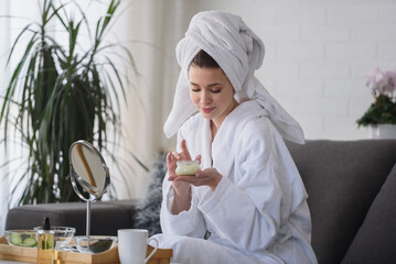 Portrait of a young beautiful woman wearing a bathrobe at home. doing her daily skincare routine with  natural cosmetics