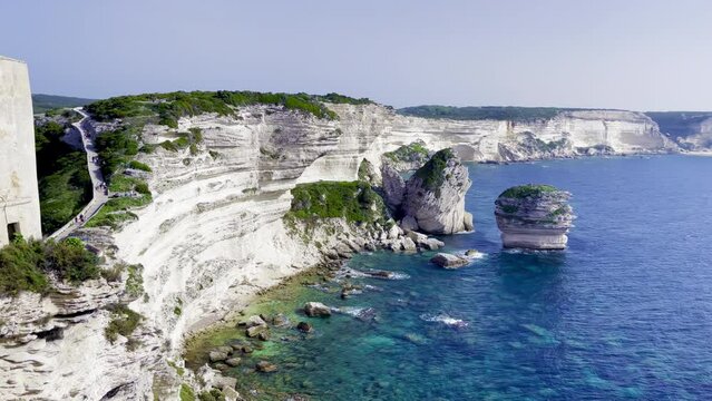 Bonifacio (Corsica, France) view of rocky cliffs of Accore coast, stack of the Grain of Sand ("U Diu Grossu" in Corsican, a big rock in the blue sea), hiking climbing path, with seagulls flying ahead