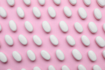 Many white dragee candies on pink background, flat lay
