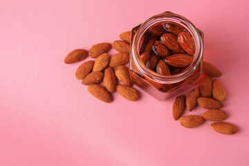 Jar with almonds and honey on pink background, above view. Space for text