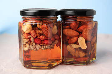 Jars with different nuts and honey on beige background, closeup