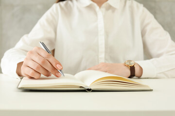 Woman writing in notebook at white table, closeup